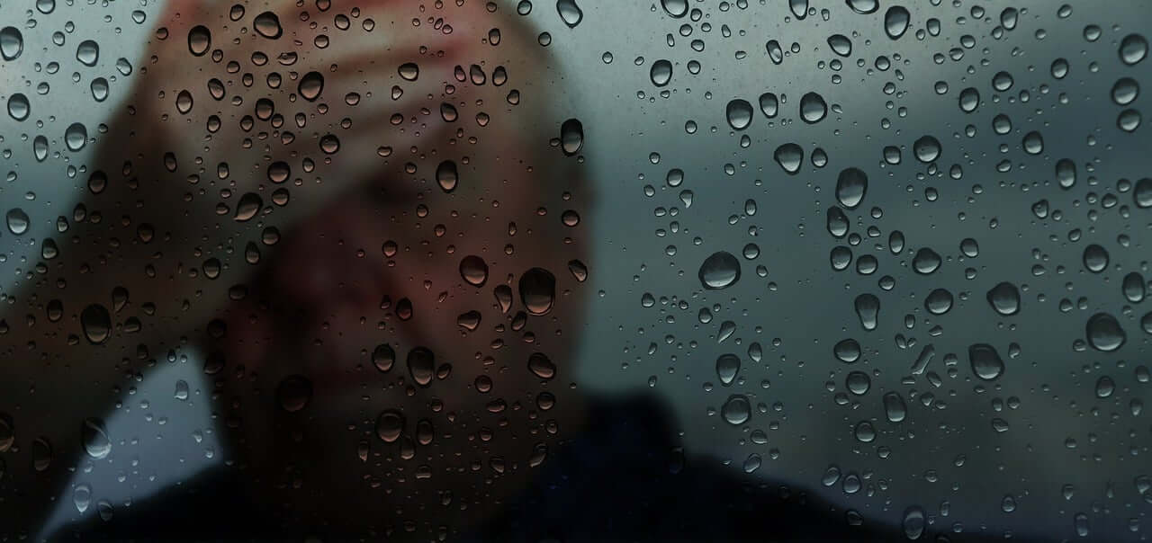homme souffrant derrière une fenêtre sous la pluie