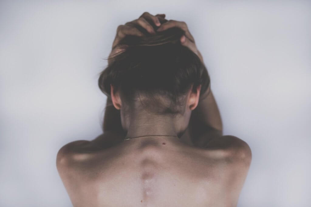 Femme de dos qui se tient la tête face à la douleur